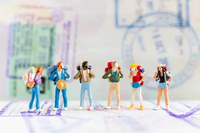 Grupo de viajeros en miniatura en medio de un pasaporte que representan la responsabilidad de la persona que diseña los viajes de autor.