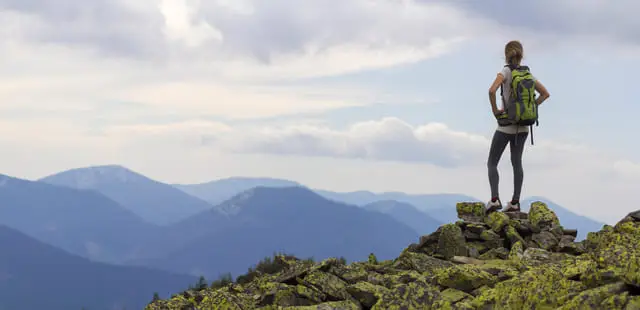 Chica en la cima de una montaña que está orgullosa por organizar viajes en grupo inolvidables.